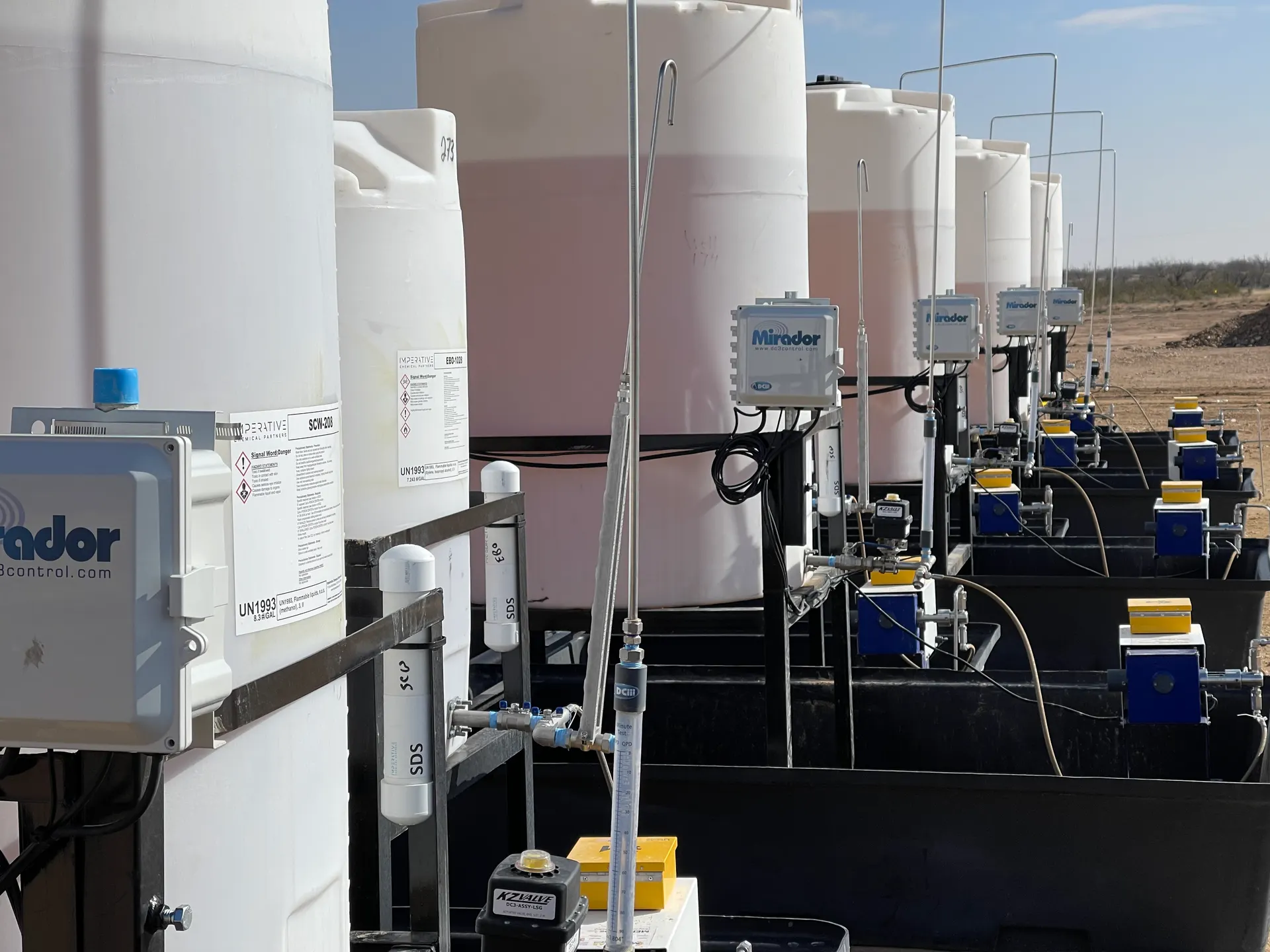 Row of chemical tanks in the field, each with a Mirador controller and injection pump